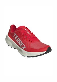 Scarpe da trail running Adidas Terrex rosse con suola bianca e grande logo Terrex bianco sui lati, vista frontale angolata su sfondo bianco.