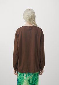 Braunes Langarmhemd aus weichem Baumwollstoff, mit einem runden Halsausschnitt und lockerer Passform, kombiniert mit einem grünem Batikrock.