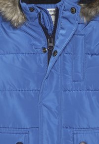 Sinivärvi pehmendatud jakk, millel on karvaga ääristatud kapuuts, tõmblukk ja nööbid. Omab kudumise tekstuuri ja esipocketipindu.