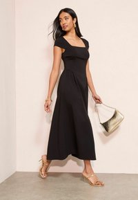 Mustast midi pikkusega kleit lühikeste varrukatega, ruudukujulise kaelusega, vöökohast sissevõetud ja voolava seelikuga. Aksessuaarideks kuldsed sandaalid ja metallik käekott.