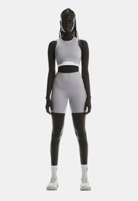 Top de sport court gris clair et shorts taille haute, design sans coutures, tissu extensible, accompagnés de chaussettes de sport blanches et de chaussures.