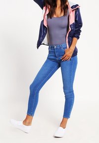 Tighta blå jeans i denim, tillsammans med en grå linne och en marinblå vindjacka med rosa detaljer. Vita sneakers fulländar looken.