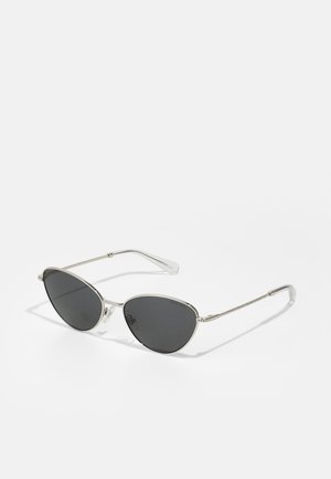 Lunettes de soleil cat-eye avec verres foncés, monture en métal argenté, accents texturés sur les branches et embouts transparents. Design minimaliste et forme élégante.