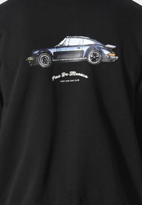 Felpa nera con un grafico di una macchina sportiva blu sul retro, con il testo "Pas De Monaco" e "NINE ONE ONE CLUB" in bianco sottostante.