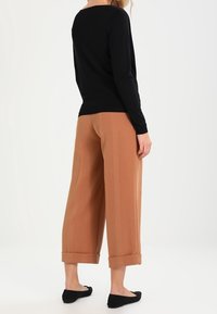 Czarna bluzka z długim rękawem, luźny krój, zestawiona z jasnobrązowymi spodniami w klasycznym kroju z wysokim stanem i podwiniętymi mankietami, dołączona do czarnych balerinek.