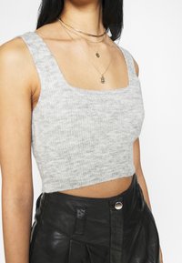 Szary dzianinowy krótki top z kwadratowym dekoltem, o miękkiej strukturze. Noszony z czarnymi, skórzanymi spodniami z wysokim stanem oraz warstwowo nałożonymi złotymi naszyjnikami.