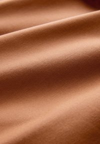 Gros plan d’un tissu lisse brun clair avec de doux plis et une texture douce visible sous un éclairage naturel.