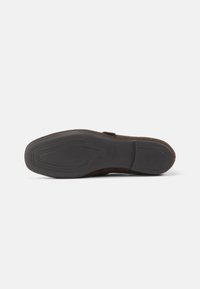 Sole di scarpa in suede marrone con battistrada in gomma nera texture. Leggera curvatura nella forma, con una finitura liscia e senza motivi o elementi in vista.