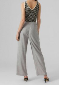 Débardeur rayé noir et blanc avec un décolleté en V, associé à un pantalon large gris clair. Comprend deux poches arrière et une coupe ajustée.