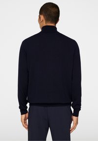 Dunkelblaues Strickpullover mit hohem Kragen und langen Ärmeln, hat eine glatte Textur und gerippte Bündchen, von hinten gesehen.
