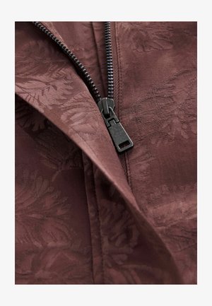 Pruun kangas peene lehe mustriga, millel on must tõmblukk ja libiseja avamisel. Tekstuuriga pind ja siledad äärised.