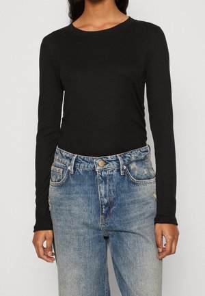 Personne portant un haut noir moulant à manches longues et un jean bleu délavé taille haute avec un bouton et des passants pour ceinture.