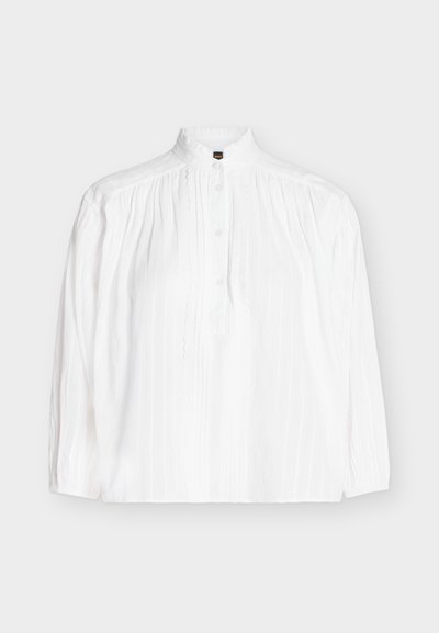 Blusa blanca de manga larga con cuello alto, tapeta de botones y detalles verticales de pliegues y encaje en la parte delantera.