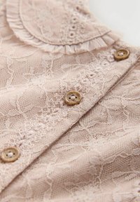 Mäkká ružová čipkovaná tkanina s kvetinovým vzorom, drevenými gombíkmi a volánikovým okrajom goliera.