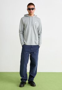 Sivá potlačená mikina s dlhým rukávom a predným vreckom, spojená s tmavomodrými cargo nohavicami so vreckami a zlatými akcentmi. Čierne topánky dopĺňajú outfit.