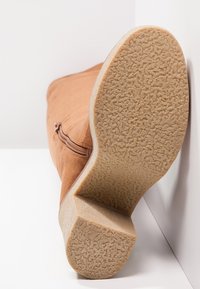 Botte haute jusqu'au genou en daim marron avec une semelle en caoutchouc texturée. Dotée d'une fermeture éclair latérale et d'un talon bas épais. Surface supérieure lisse.