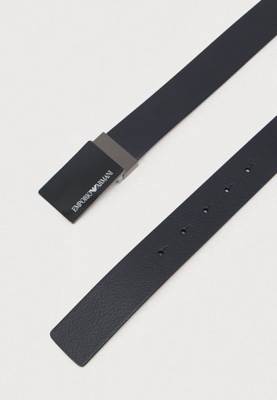 Tumši zils ādas jostas ar taisnstūra formā melnu metāla sprādzi, uz kuras ir teksts "Emporio Armani", trīs regulēšanas caurumi un gluda tekstūra.