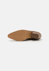 Zapato de tacón marrón con un acabado texturizado, que presenta una suela de goma lisa y un diseño de punta afilada. Los acentos incluyen sutiles detalles florales.