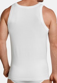 Hvid bomulds tanktop med en glat tekstur, ærmeløs design og rund halsudskæring, vist fra ryggen med en tætsiddende form.