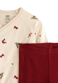 Kläder för babyn i bomull med en krämfärgad topp med skogstryck och ett par röda ribbade byxor. Toppen har V-ringning och en mjuk textur.