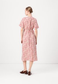 Rochie midi cu imprimeu floral, cu un model roz, mâneci scurte și o talie accentuată cu detaliu legat. Asortată cu pantofi cu toc maronii.