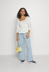 Top peplum de estampado floral, azul claro, com mangas bufantes; usado com jeans azul claro e uma pequena bolsa amarela com detalhes coloridos.