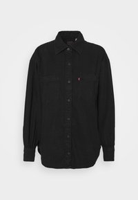 Schwarzes Hemd zum Zumachen mit langen Ärmeln, zwei Brusttaschen und einem Kragen aus strukturiertem Stoff. Verfügt über elastische Bündchen.