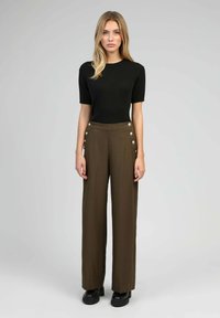 Top noir à rayures côtelées à manches courtes associé à un pantalon marron taille haute à jambes larges avec de grands boutons décoratifs sur les côtés. Chaussures à plateforme noires.