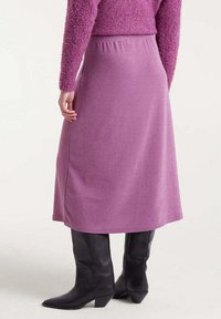 Falda midi morada hecha de una tela suave con cintura elástica, que presenta una textura lisa y una silueta recta, combinada con botas negras de tacón.