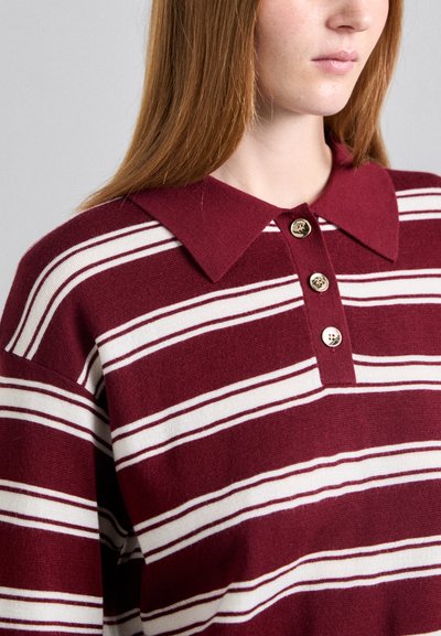 Maroon ja valkoinen raidallinen polo-paita, jossa on kaulus, kolme pyöreää nappia ja teksturoitu neulekangas.