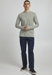 Langærmet, lysegrå henley skjorte med tre-knaps placket, parret med marineblå cargo bukser med sidelommer. Båret med sorte sneakers.