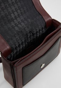 Brun læder håndtaske med en tekstureret overflade og sort mønstret indvendig. Har en klaplukning og en forlommes med en metalsnap.