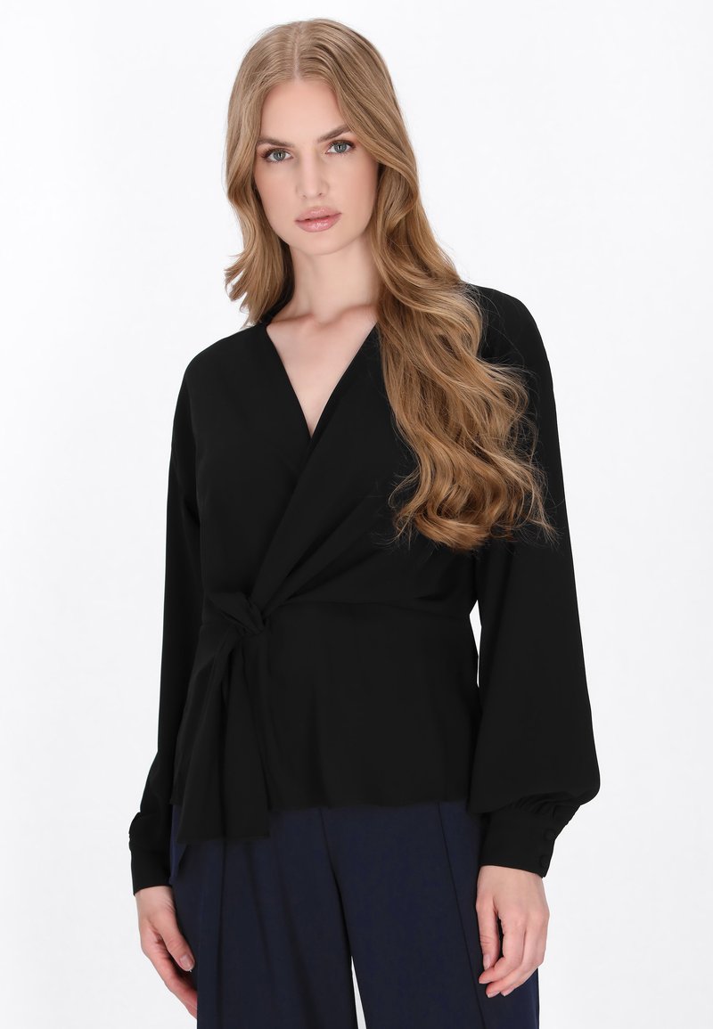 Zwarte wikkelblouse met lange, ballonmouwen en een strikdetail in de taille. Zachte stof met een gladde textuur, voorzien van een diepe V-hals.