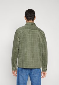 Grøn corduroy skjorte med et rutenet mønster, knaplukning ved manchetterne og spredt krave, parret med blå denim jeans.