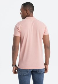 Polo-paita, vaaleanpunainen, lyhyet hihat, ribbireunus, teksturoitu kangas; käytetty farkkujen kanssa, näkymä takaa.