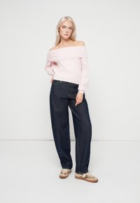 Απαλή ροζ ζακέτα με ανοιχτούς ώμους και ραμμένο γιακά, συνδυασμένη με σκούρα τζιν παντελόνια σε φαρδιά γραμμή που διαθέτουν διακοσμητικά πλάγια και τσέπες.