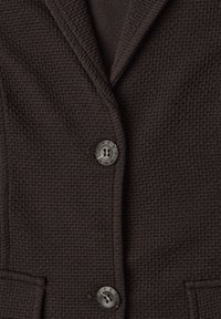 Tissu de blazer marron foncé texturé avec deux boutons noirs et un col à revers cranté visible.