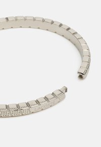Bracciale in metallo con un design segmentato, caratterizzato da una finitura argentata lucida e dal logo "LACOSTE" inciso con accenti puntinati su alcuni segmenti.
