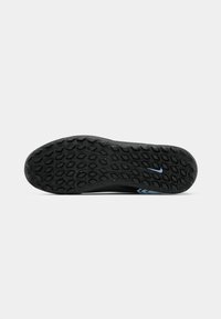 Suola di scarpa sportiva nera con motivo testurizzato per grip; presenta un piccolo accento blu vicino al tallone e una superficie in gomma liscia e resistente.