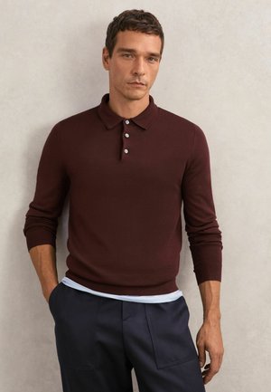 Bordowy sweter polo z dzianiny z długimi rękawami, kołnierzem na zakładkę i trzema guzikami oraz ciemnymi spodniami.