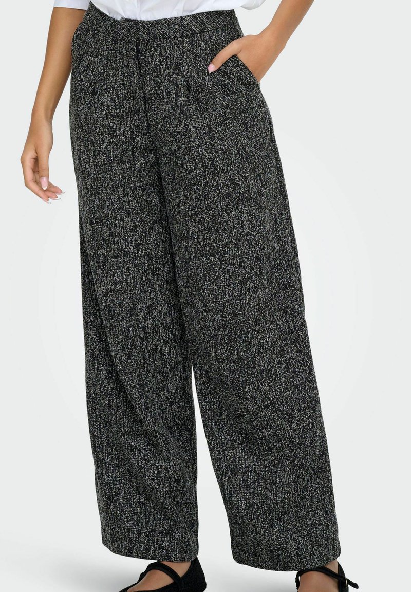 Pantaloni a gamba larga in tessuto texturizzato bianco e nero, caratterizzati da una vestibilità comoda e tasche laterali, abbinati a calzature nere.