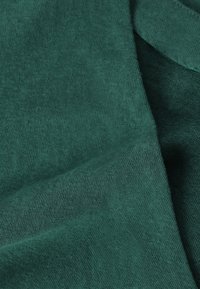Gros plan sur un tissu vert foncé texturé avec un motif tricot visible et des plis doux.