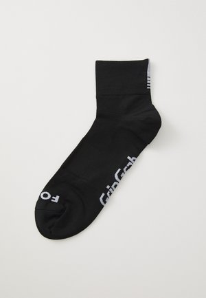 Calcetín negro de textura suave, con diseño de longitud hasta el tobillo, que presenta una marca blanca en el costado y tres franjas horizontales en la parte superior.