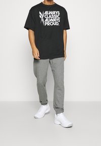 Černé tričko s bílým potiskem, v kombinaci se šedými tepláky. Model má na sobě bílé sportovní boty. Jednoduchý, ležérní outfit.