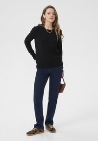 Maglione nero a maniche lunghe, jeans dritti blu scuro, sneakers con stampa leopardata, in mano una piccola borsa marrone. Outfit semplice e casual.