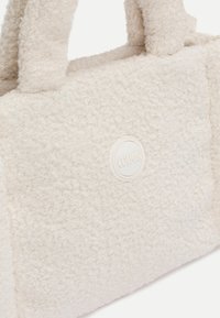 Weichtexturiertes weißes Handtasche mit kurzen Griffen und einem runden Logo-Patch mit der Aufschrift "COLMAR" auf der Vorderseite.