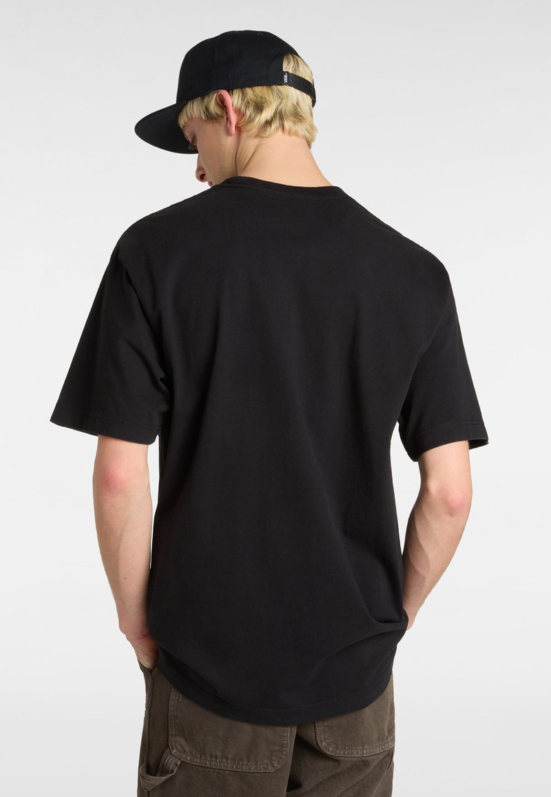 T-shirt en coton noir à manches courtes, col rond et coupe décontractée. Porté avec un pantalon cargo gris et une casquette noire.