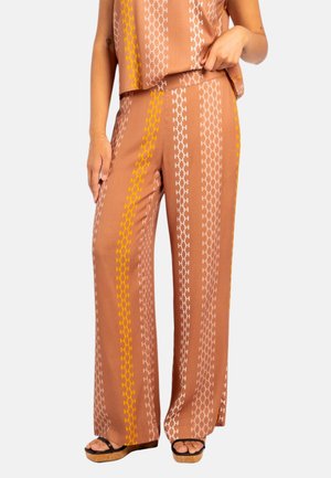 Brune vide bukser med vertikale hvite og gule kjedelinkmønstre, båret med matchende topp og svarte kilhæl-sandaler.