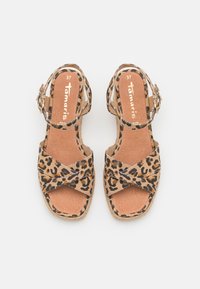 Sandale imprimée léopard avec des brides en tissu croisées, une boucle à la cheville et un talon compensé beige. Matériau en faux suedine avec une semelle intérieure douce et texturée.