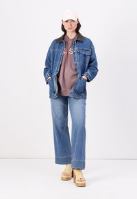 Denim jakna s temnim ovratnikom, prevelik dizajn; rjav pulover z besedilom; široke modre kavbojke; bež platforme; svetlo roza kapa.